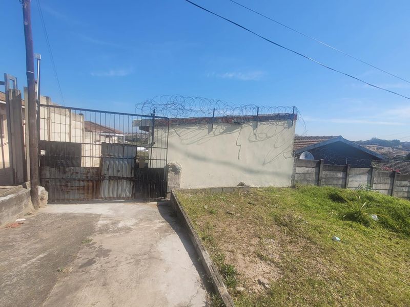 Front exterior view of the property featuring a metal security gate, perimeter wall with razor wire, and a concrete driveway.