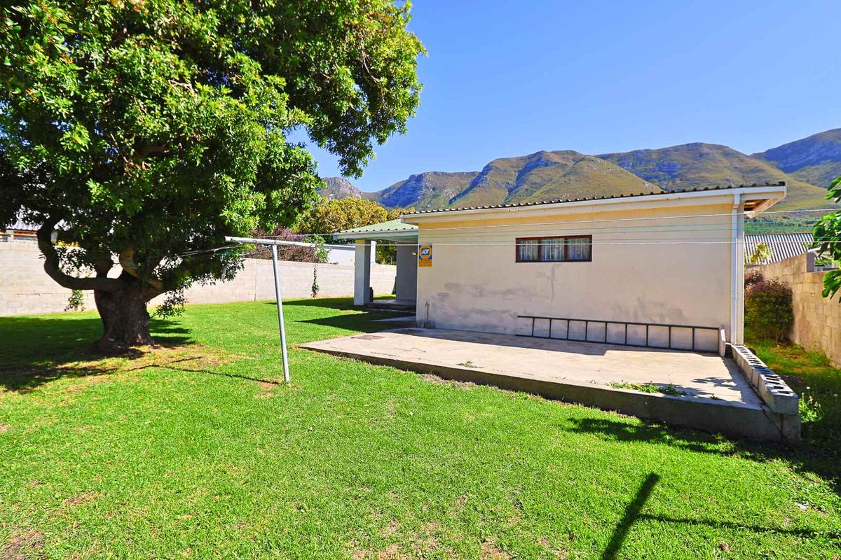 Rear view of the property featuring a concrete patio, lawn area, and perimeter wall with mountain views in the background.