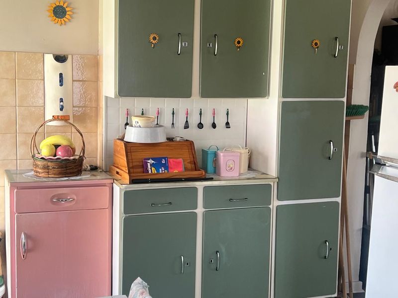 A dated kitchen featuring vintage-style built-in cabinetry with a mix of green and pink finishes and a tiled backsplash.