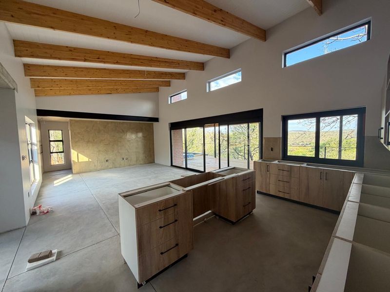 Spacious open-plan living and kitchen area featuring exposed timber beams, polished concrete floors, and large sliding doors leading to an outdoor deck.