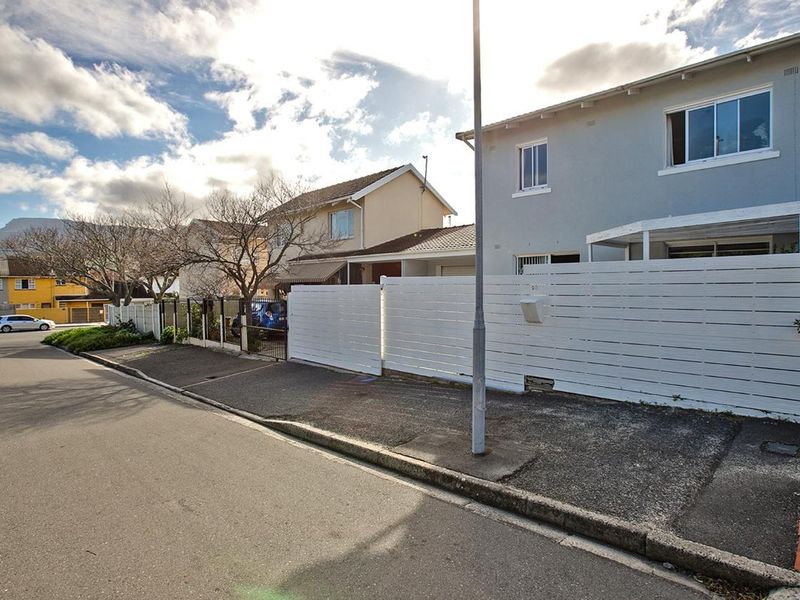 Street view of the property showing the front facade, white timber fencing, and paved driveway access.