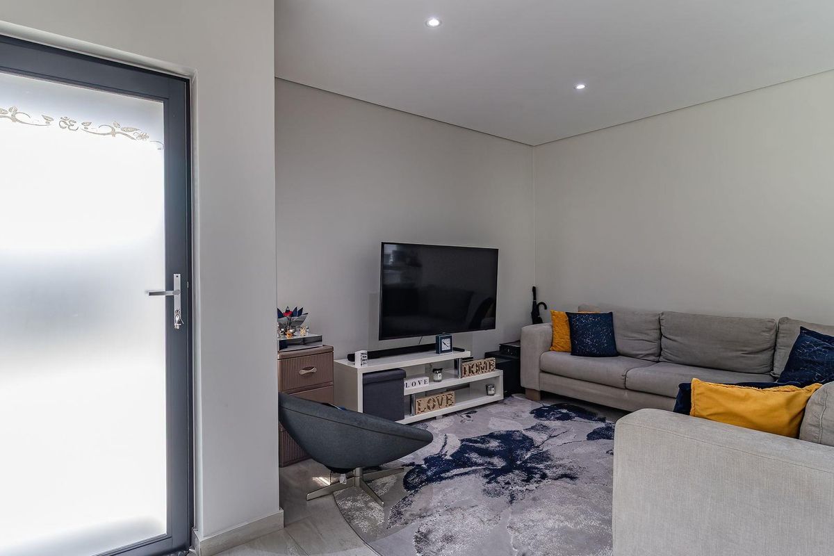A well-maintained living room featuring recessed downlights, tiled flooring, and a modern frosted glass door leading to the exterior.