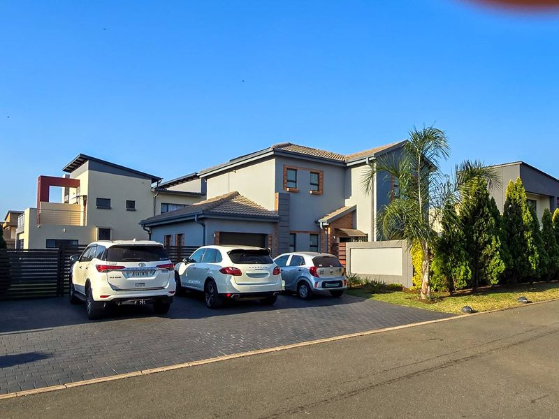 Front elevation of a modern double-story house featuring a paved driveway, tiled roof, and landscaped garden area.