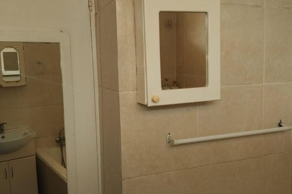 A functional bathroom featuring tiled walls, a wall-mounted medicine cabinet, and a towel rail, with a mirror reflecting the vanity and bathtub area.