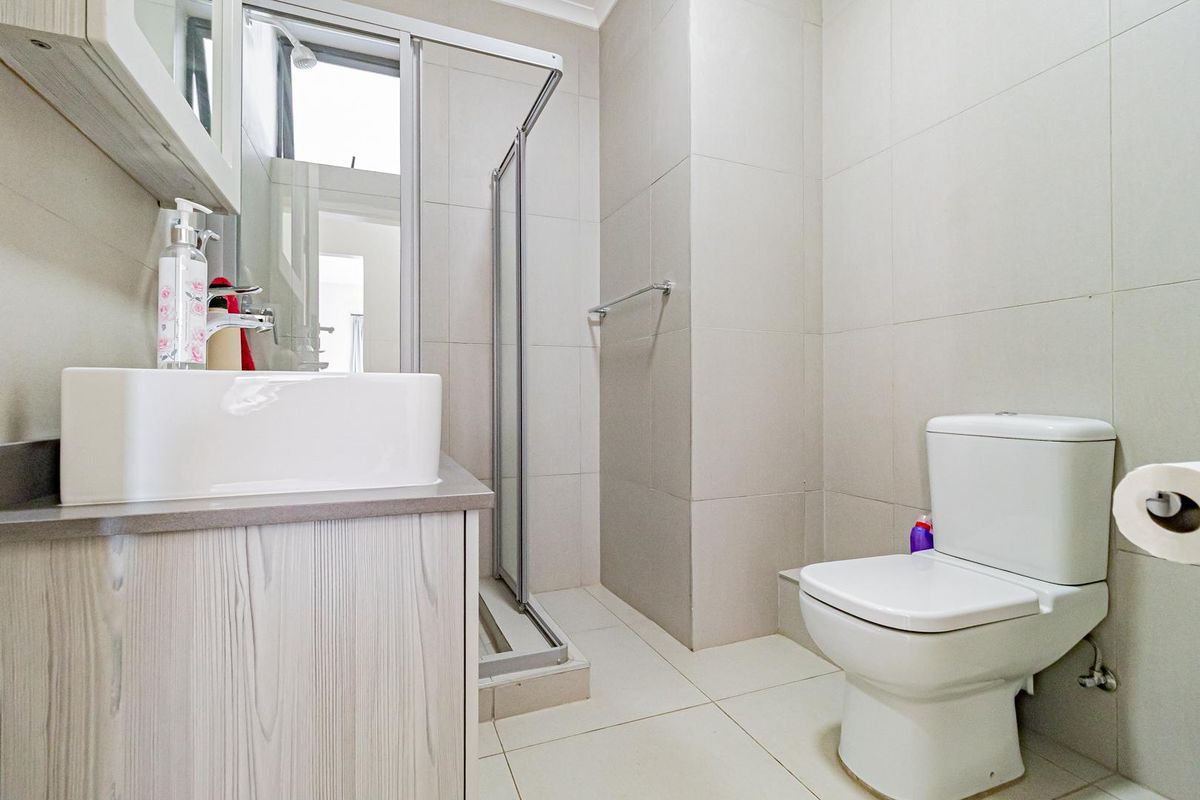 A clean and functional bathroom featuring a modern vanity, a glass-enclosed shower, and neutral floor-to-ceiling tiling.