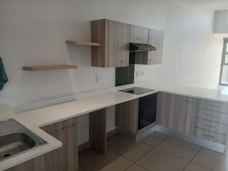 Modern kitchen featuring light wood-grain cabinetry, stone countertops, integrated electric hob, oven, and extractor fan, complemented by sleek tiled flooring.