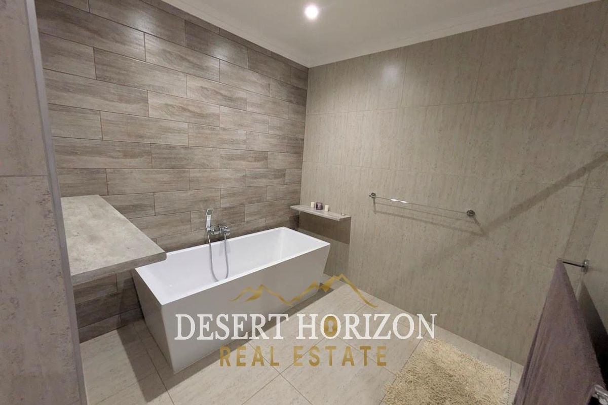 Modern bathroom featuring a freestanding bathtub, neutral wall tiling, and a built-in stone shelf.