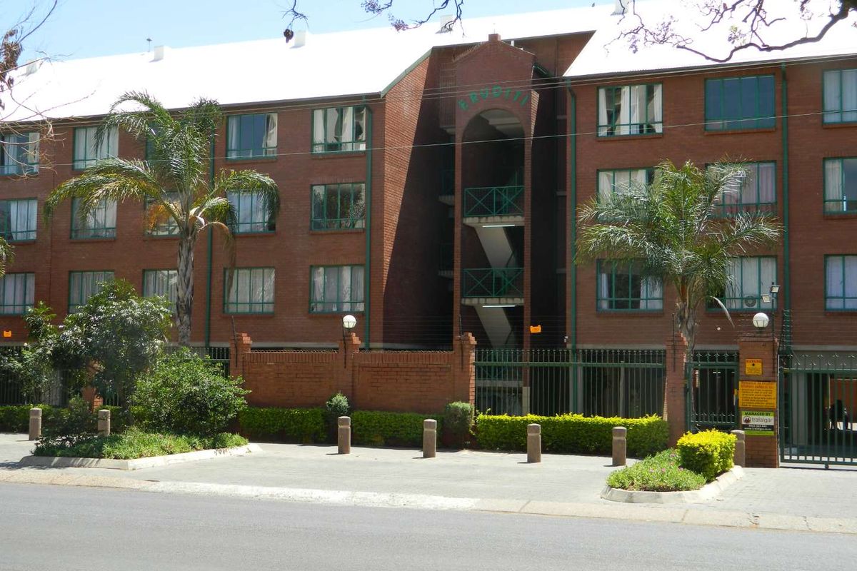 Front elevation of a multi-story brick apartment complex featuring secure gated access, paved driveway, and external stairwell architecture.