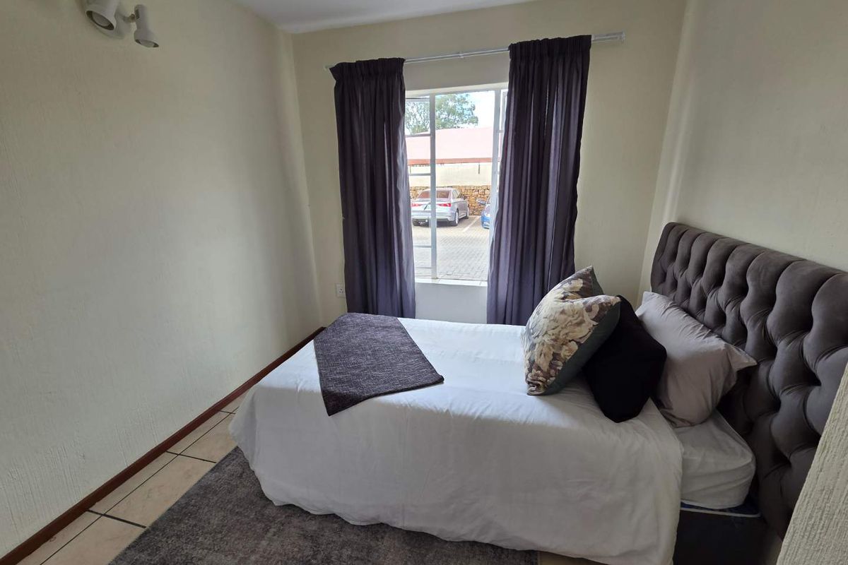 A compact bedroom featuring tiled flooring, neutral wall finishes, and a window with curtain tracks, providing a functional living space.