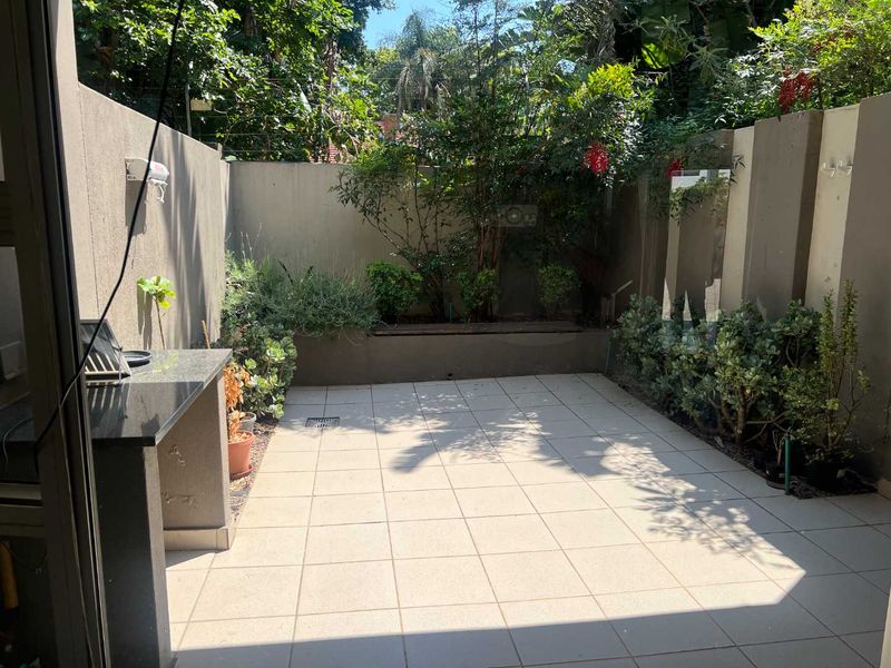 A private, paved patio area featuring a built-in granite countertop and a raised garden bed, perfect for outdoor entertaining.