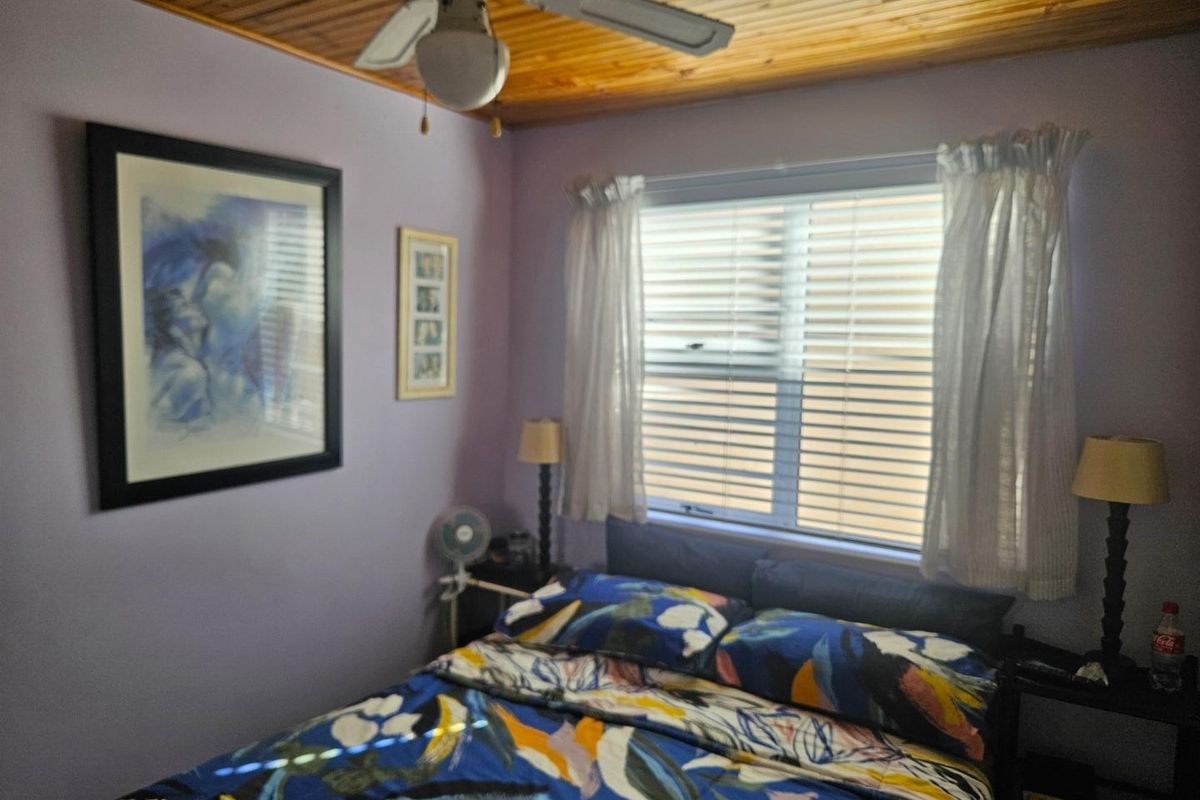A cozy bedroom featuring a timber-paneled ceiling, a ceiling fan, and a window with fitted blinds.