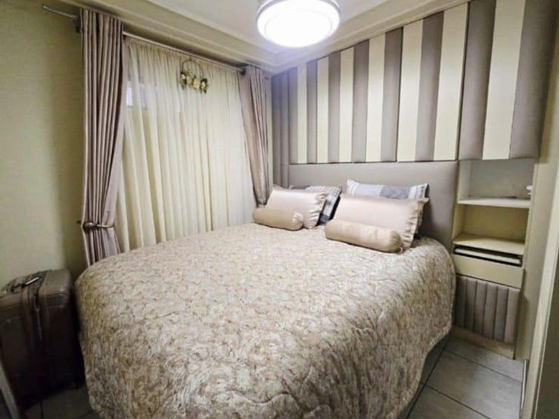 A compact bedroom featuring custom built-in cabinetry and a headboard wall, finished with neutral tones and tiled flooring.