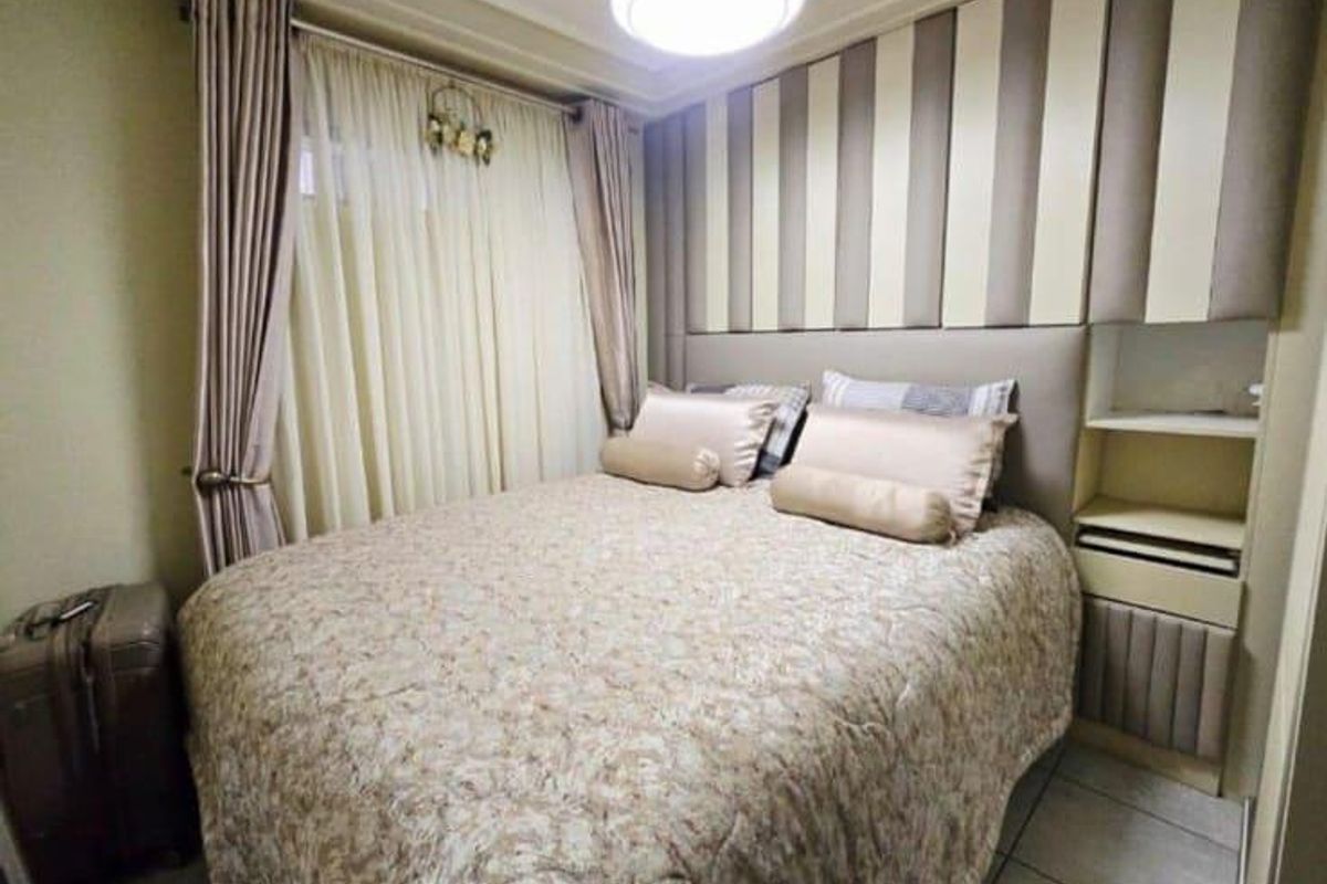 A compact bedroom featuring custom built-in cabinetry and a headboard wall, finished with neutral tones and tiled flooring.