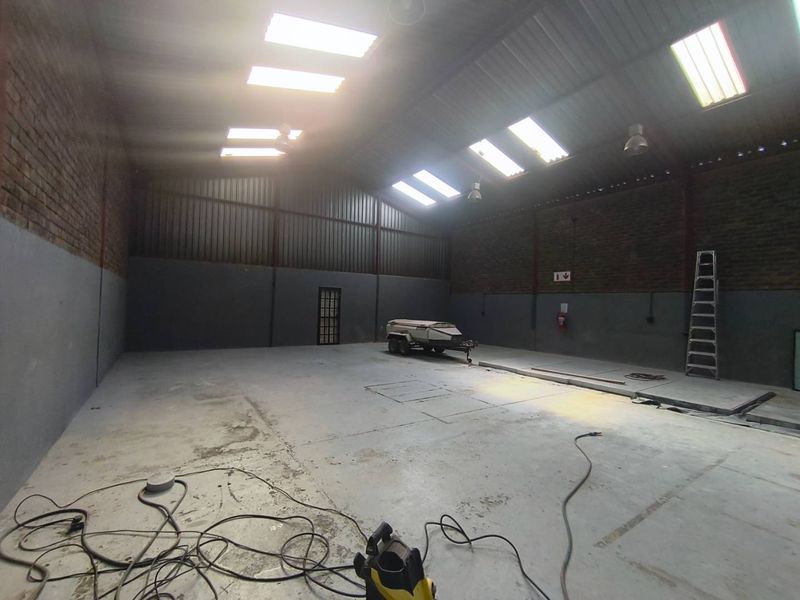 Spacious industrial utility area featuring high ceilings with skylights, exposed brick walls, and durable concrete flooring, suitable for storage or workshop use.