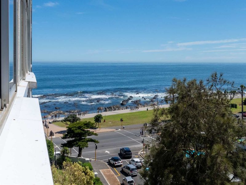 Elevated coastal view overlooking the ocean, promenade, and street intersection from an apartment window.
