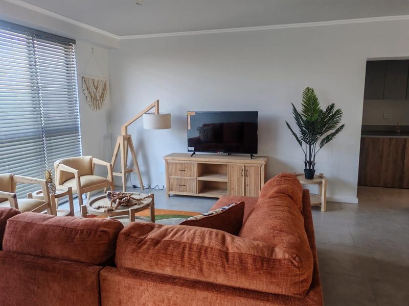 A bright and well-maintained living room featuring neutral tiled flooring, coving, and large windows fitted with venetian blinds, offering a clean and modern aesthetic.
