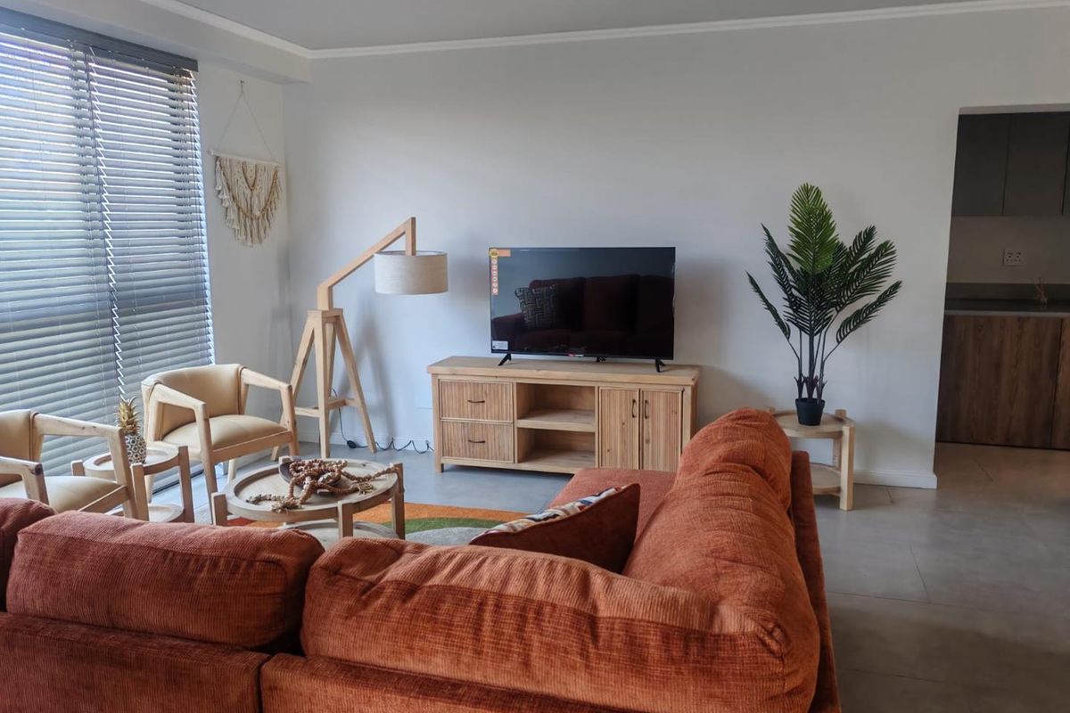 A bright and well-maintained living room featuring neutral tiled flooring, coving, and large windows fitted with venetian blinds, offering a clean and modern aesthetic.