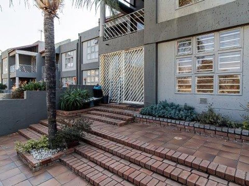 Rear exterior view of the apartment featuring a tiled patio area with brick steps, security gate, and textured facade finish.