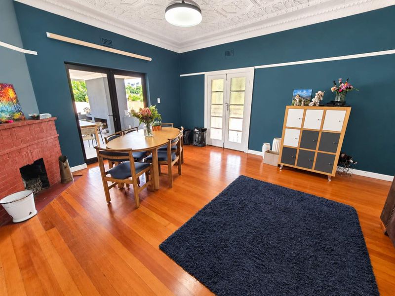 Spacious living room featuring original hardwood flooring, an ornate ceiling, a classic brick fireplace, and direct access to the outdoor patio area.