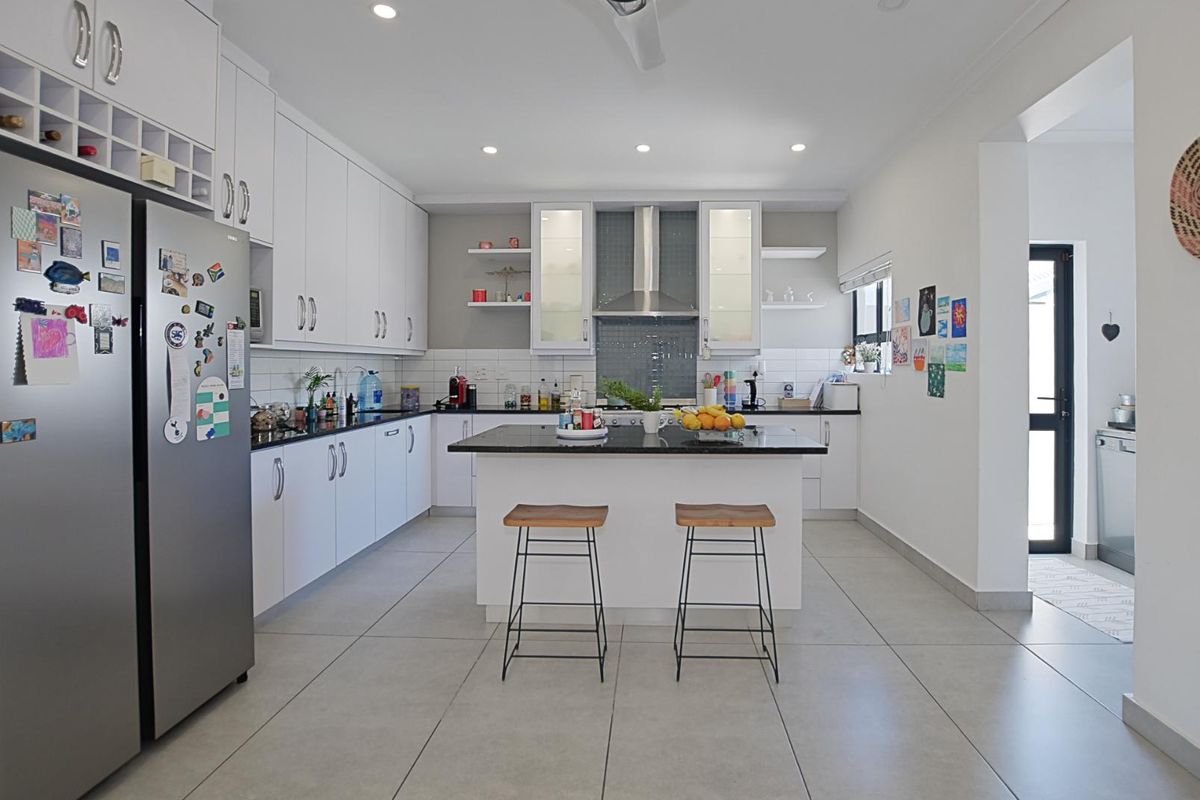 Modern kitchen featuring white cabinetry, a central island with a dark stone countertop, tiled flooring, and integrated stainless steel appliances.