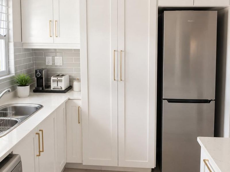Modern kitchen featuring white shaker-style cabinetry, subway tile backsplash, quartz countertops, and brushed gold hardware with integrated pantry storage.
