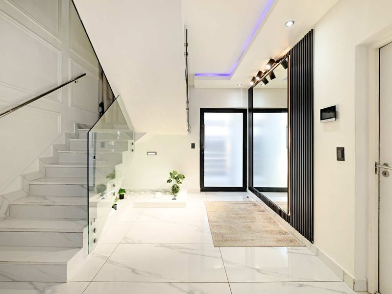 Modern entrance hall featuring marble-look floor tiles, a sleek glass balustrade staircase, and contemporary slatted wall detailing with integrated lighting.