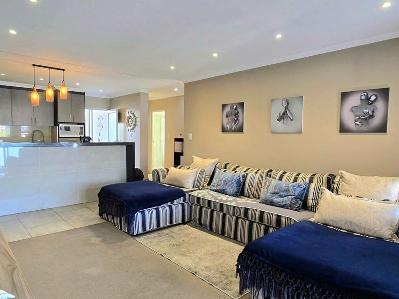 An open-plan living and kitchen area featuring a breakfast bar, recessed downlighting, and a combination of tiled and carpeted flooring.