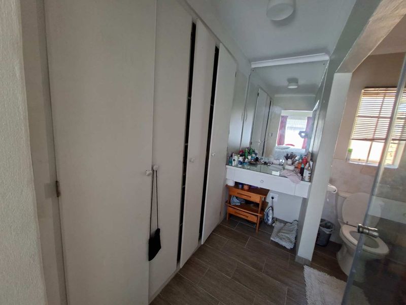 Bathroom featuring built-in cupboards, a vanity basin with mirror, toilet, and a shower enclosure with tiled flooring.