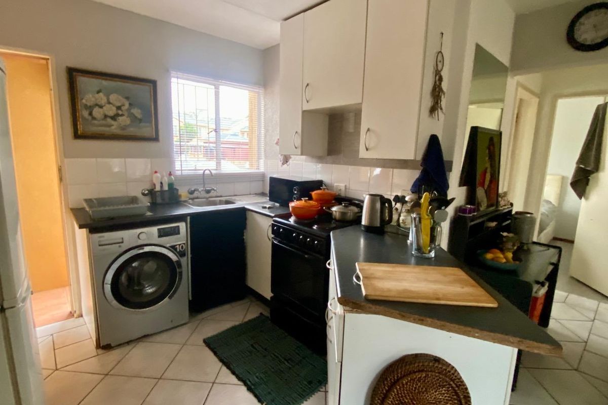 Compact kitchen featuring white cabinetry, dark countertops, tiled flooring, and integrated space for a washing machine, offering a functional layout.
