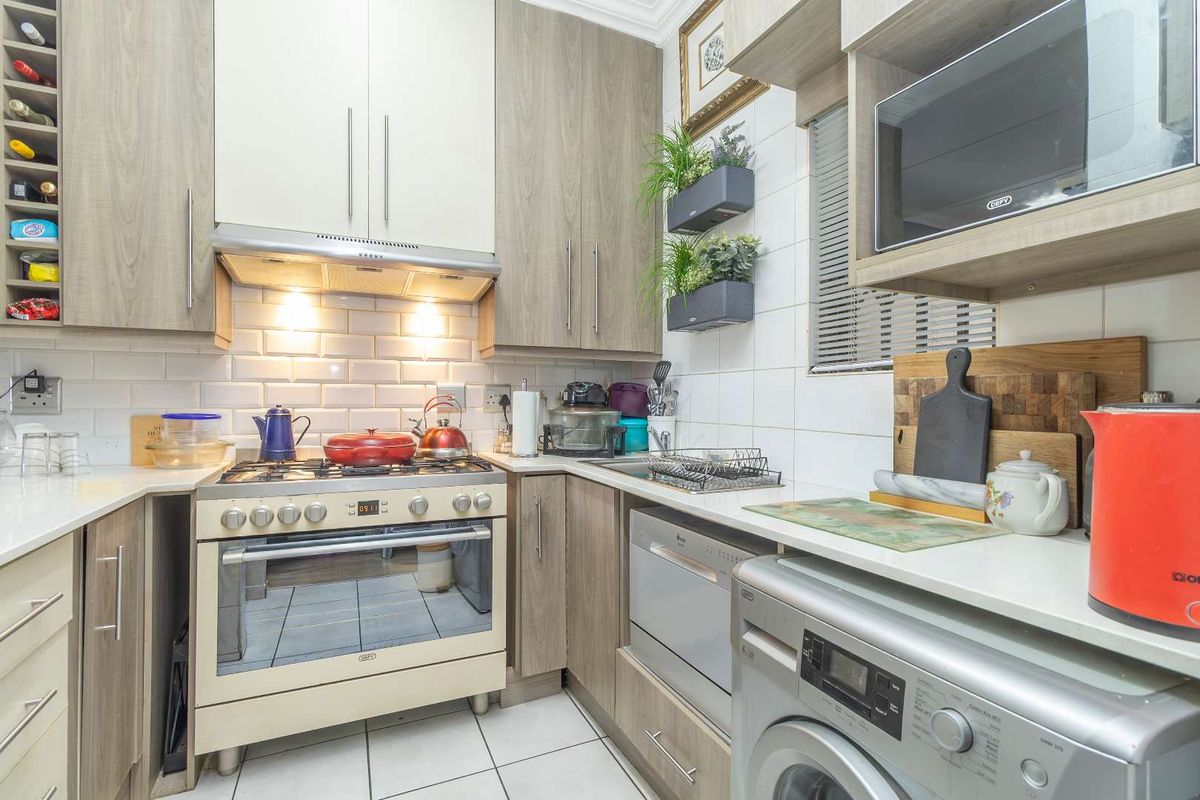 A compact kitchen featuring wood-grain cabinetry, subway tile backsplash, a gas stove with extractor fan, and integrated space for a washing machine.
