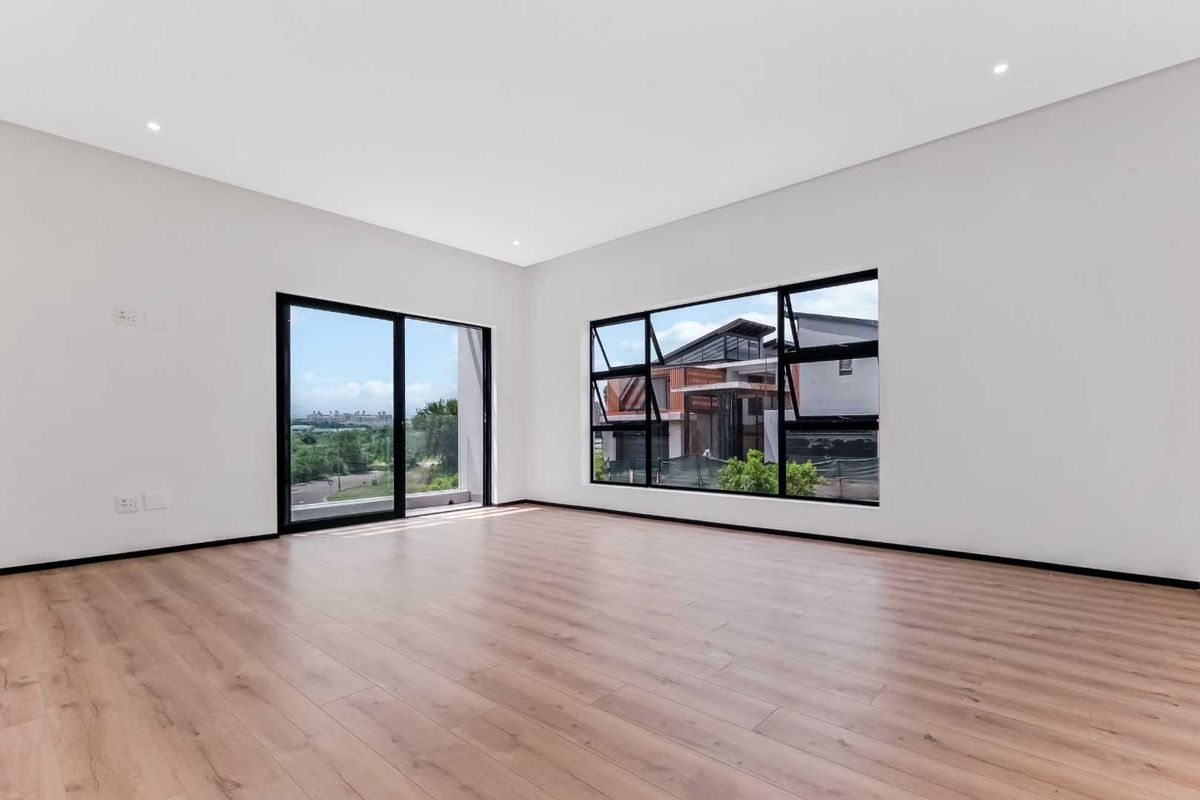 A bright, spacious, and empty bedroom featuring modern wood-look flooring, large black-framed windows, and a sliding door leading to an outdoor area.