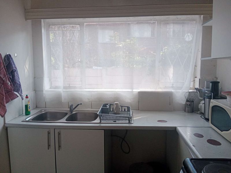 A functional kitchen area featuring a double bowl stainless steel sink, laminate countertops, and built-in base cabinetry with a tiled splashback.