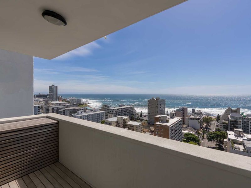A private balcony featuring timber decking and a concrete balustrade, offering expansive panoramic views of the coastline and urban cityscape.