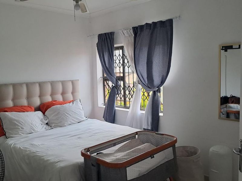 A functional bedroom featuring tiled flooring, a ceiling fan, and a window fitted with a security gate.