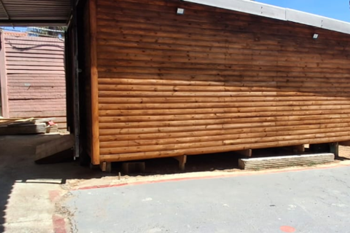 A view of a timber-clad structure with a corrugated metal roof, situated on a concrete driveway with visible surface cracking.