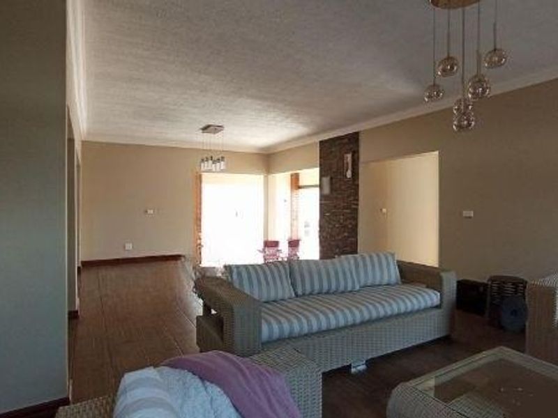 Spacious living area featuring tiled flooring, a stone feature wall, and modern pendant lighting, offering an open-plan layout with natural light.