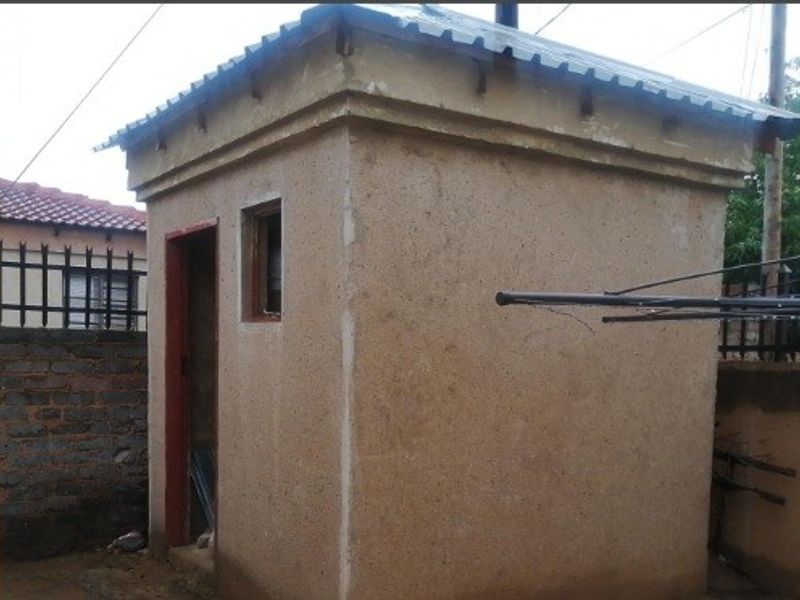 A small, detached utility structure featuring plastered walls and a corrugated metal roof, currently requiring finishing and door installation.