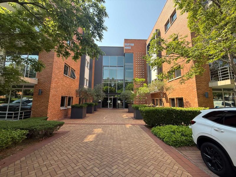 Front entrance view of Silky Oak House, featuring a modern brick and glass facade with a paved driveway and landscaped garden area.