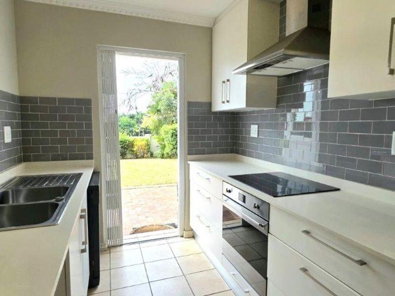 A clean, modern kitchen featuring white cabinetry, stone countertops, subway tile backsplash, and integrated appliances, with direct access to the rear garden.