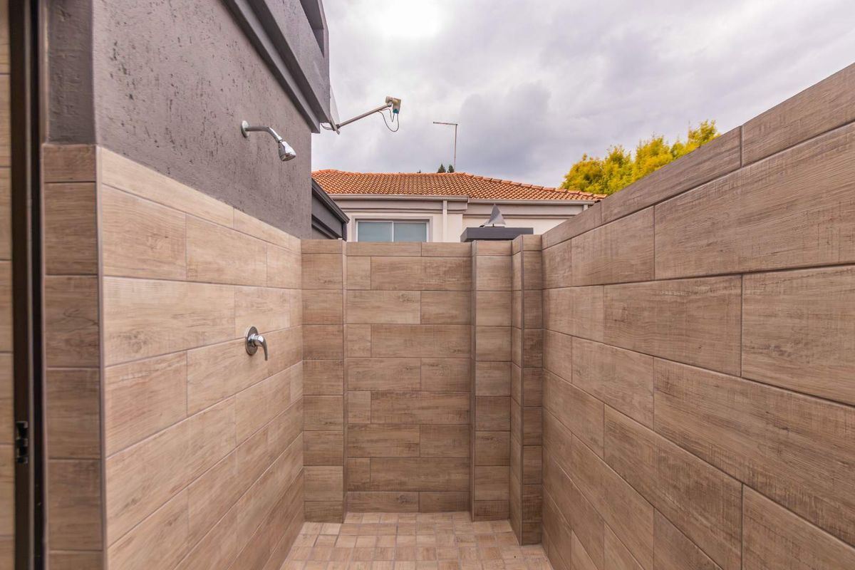 An outdoor shower area featuring modern wood-look tile cladding and durable floor tiling, providing a functional and private exterior wash space.