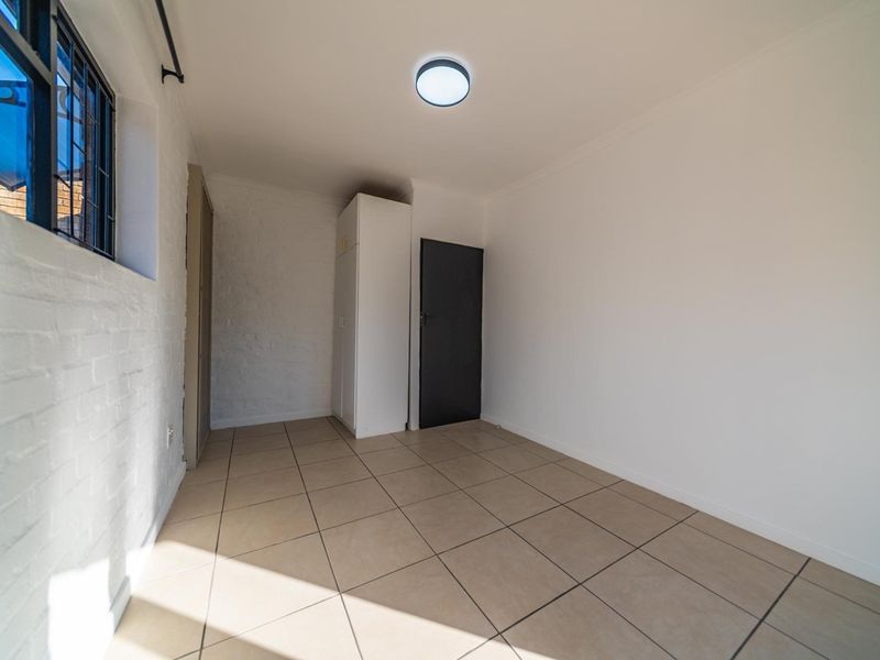 A clean, empty bedroom featuring tiled flooring, a built-in cupboard, and a window with security bars, offering a neutral space ready for personalization.