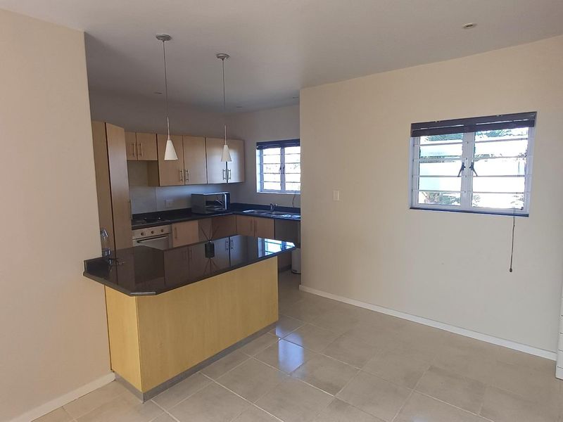 Open plan kitchen and living area featuring granite countertops, light wood cabinetry, tiled flooring, and natural light through multiple windows.