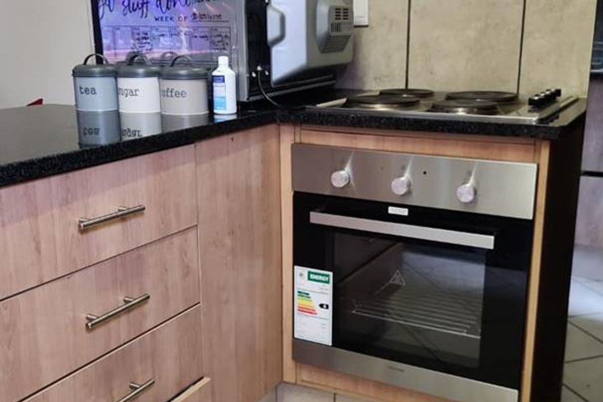 Compact kitchen corner featuring light wood-finish cabinetry, granite countertops, a built-in electric oven, and a four-plate hob with tiled splashback.