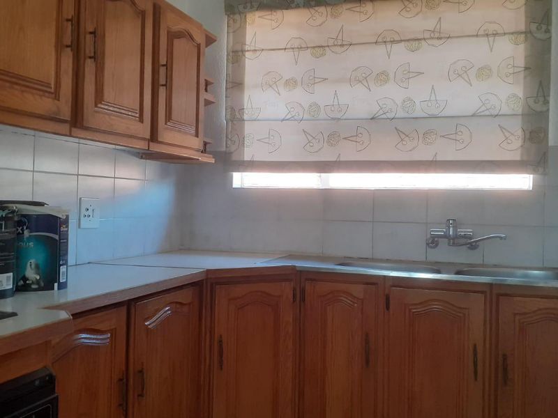 A functional kitchen featuring traditional wooden cabinetry, laminate countertops, a double bowl sink, and tiled splashbacks, offering potential for a modern renovation.