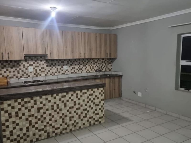 A functional kitchen featuring wood-look cabinetry, mosaic tile backsplash, built-in hob, and tiled flooring in an open-plan layout.