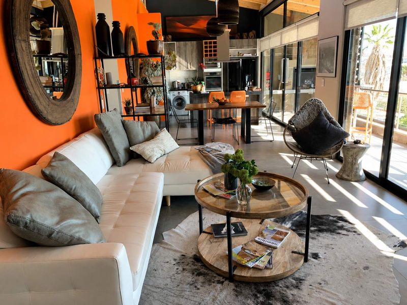 Modern open-plan living and kitchen area featuring high ceilings with exposed timber beams, sleek cabinetry, and large sliding doors leading to a balcony.