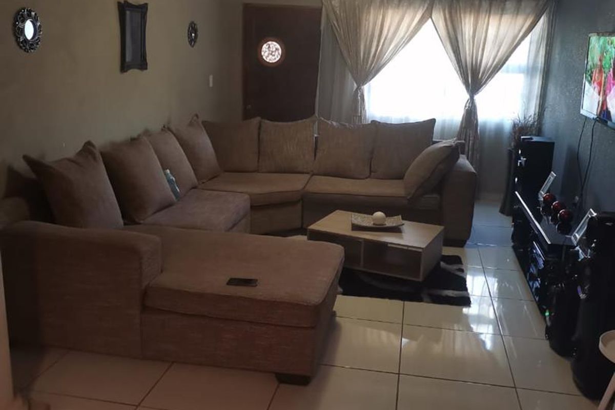 A living room featuring tiled flooring, a glossy ceiling finish, and a window with curtains.