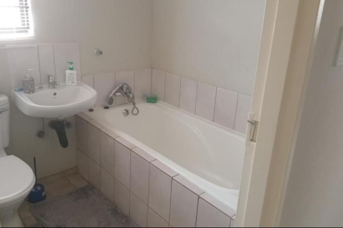 A functional bathroom featuring a built-in bathtub with tiled surround, a wall-mounted basin, and a standard toilet.