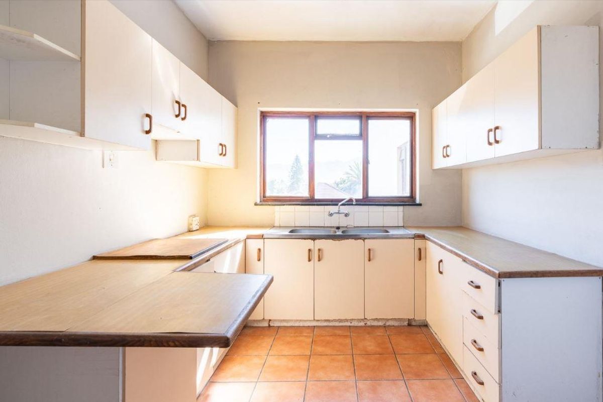 A dated kitchen featuring original cabinetry, laminate countertops, a double basin sink, and terracotta floor tiles, offering a blank canvas for renovation.