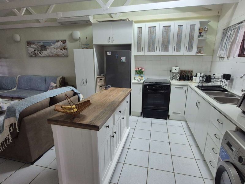 Open-plan living area featuring a kitchen with white cabinetry, a wooden-topped island, tiled floors, and exposed roof trusses, creating a functional and connected space.